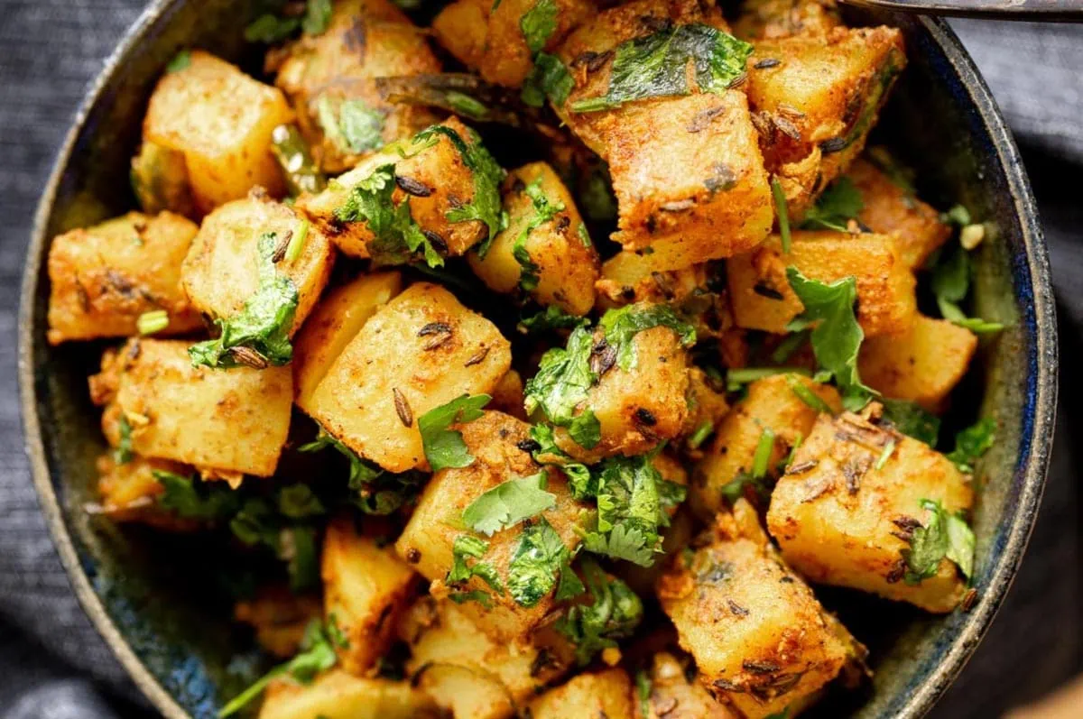 cumin spiced potatoes served in a white bowl sprinkled with coriander