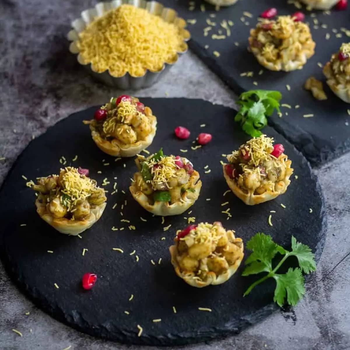 close up shot of aloo chana chaat placed in black slate board with sev on the side