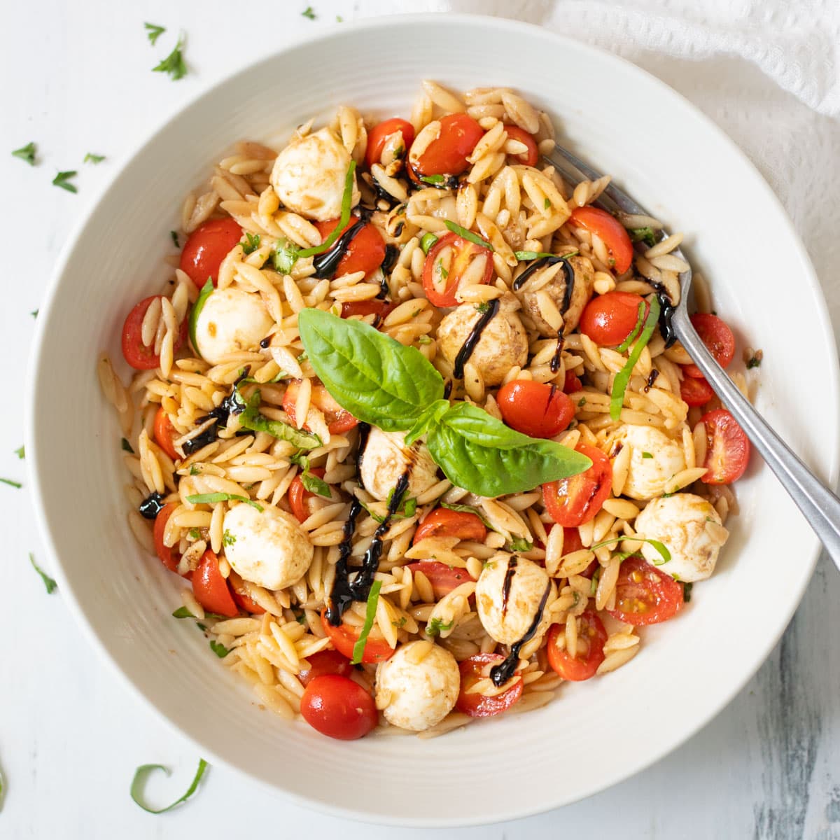 Caprese orzo pasta salad in a bowl garnished with basil leaves