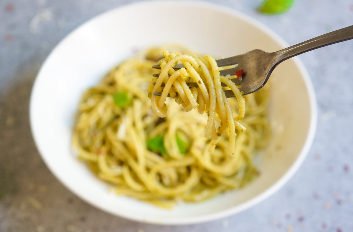 Spaghetti Pesto in a fork over a white bowl 