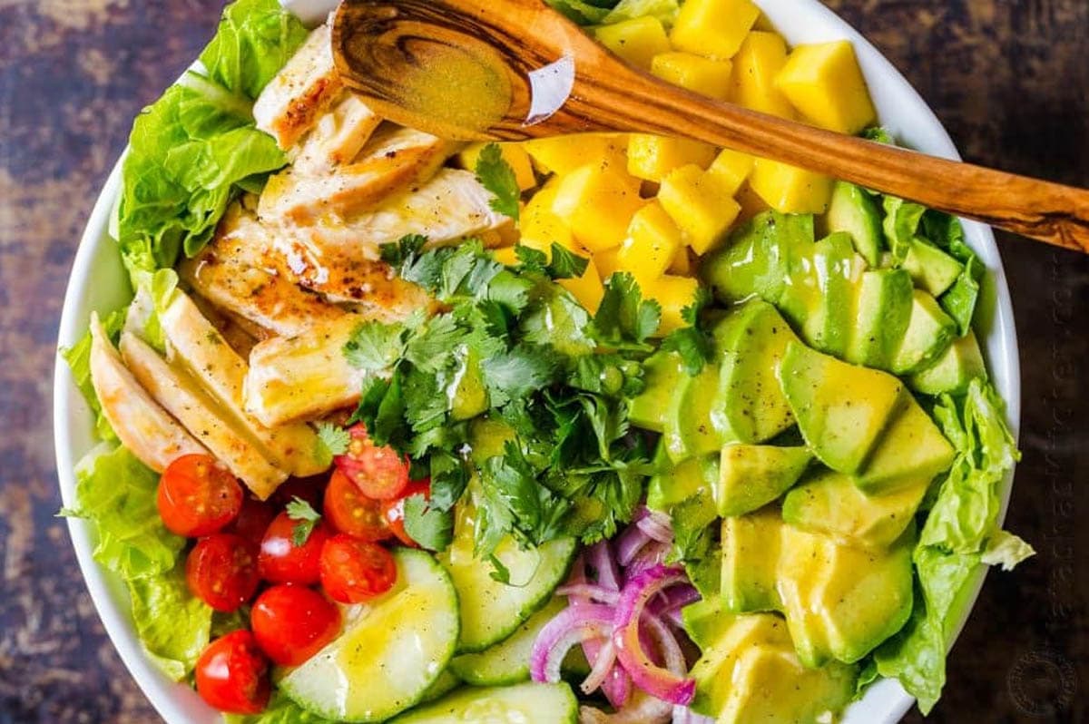 Ingredients for chicken mango avocado salad arranged in bowl with spoon