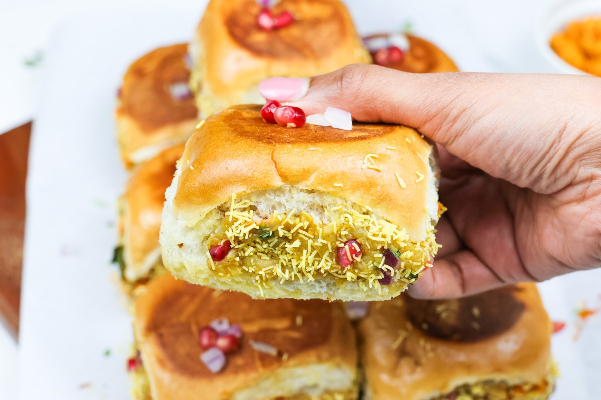 Dabeli in hand garnished with pomegranate seeds and sev