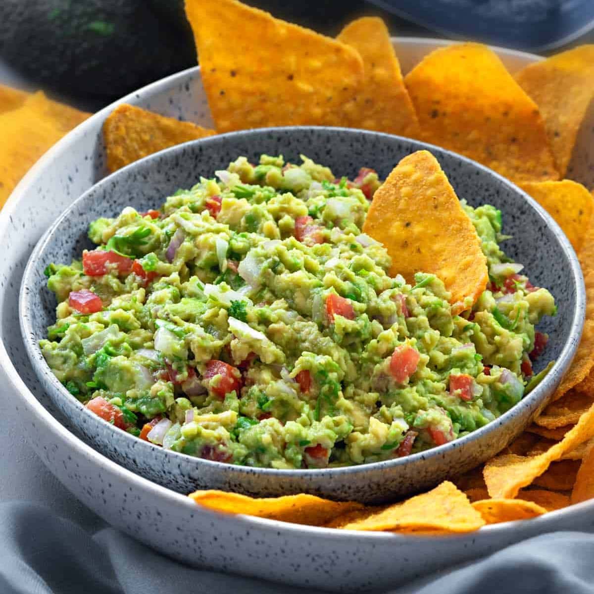 close up of a bowl filled with homemade guacamole with a platter of yellow tortilla chips
