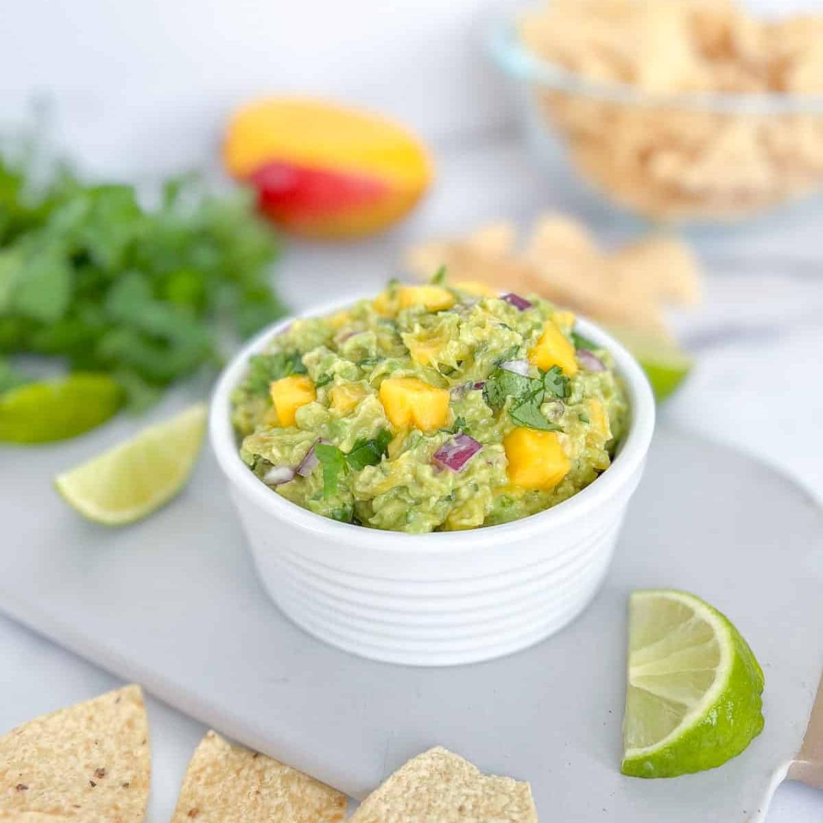 Mango guacamole in a bowl with lime wedge and tortilla chips.