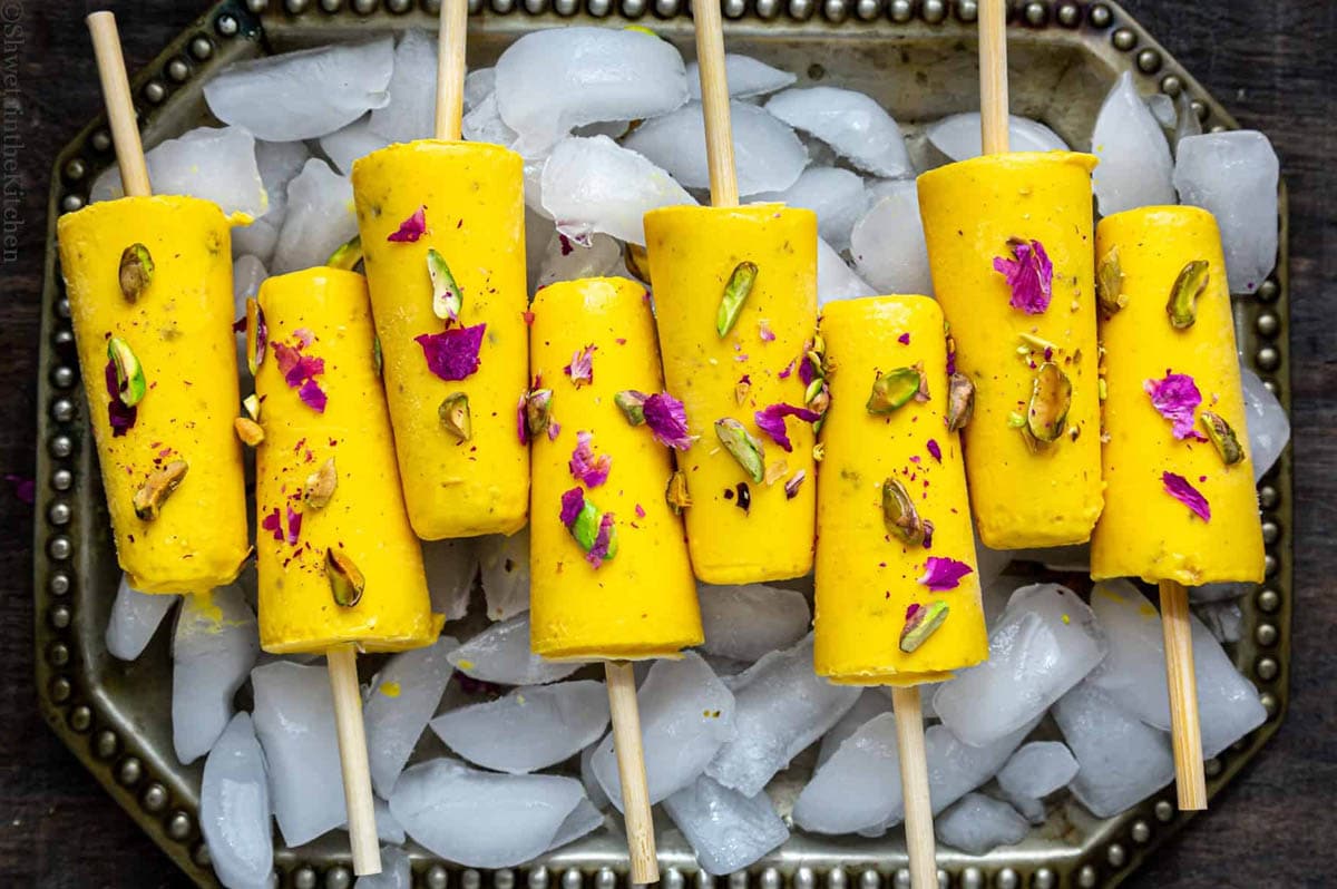 8 Mango Kulfis on a ice filled tray topped with pistachios and dry rose petals