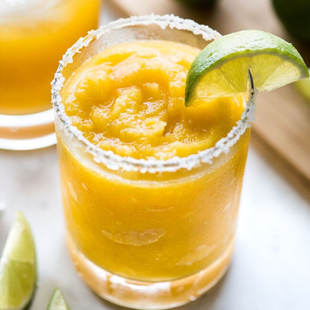 A mango margarita served frozen with a lime wedge.