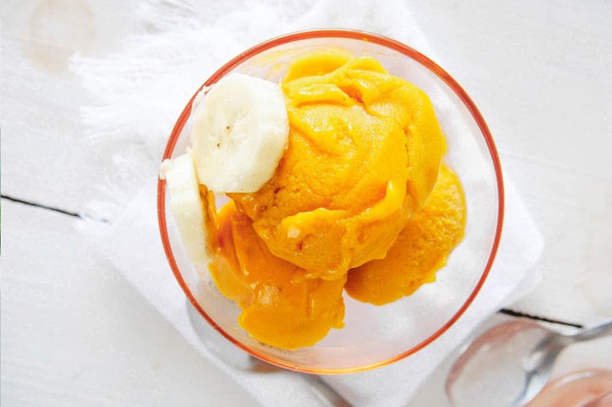 mango nice cream in a glass container with sliced bananas