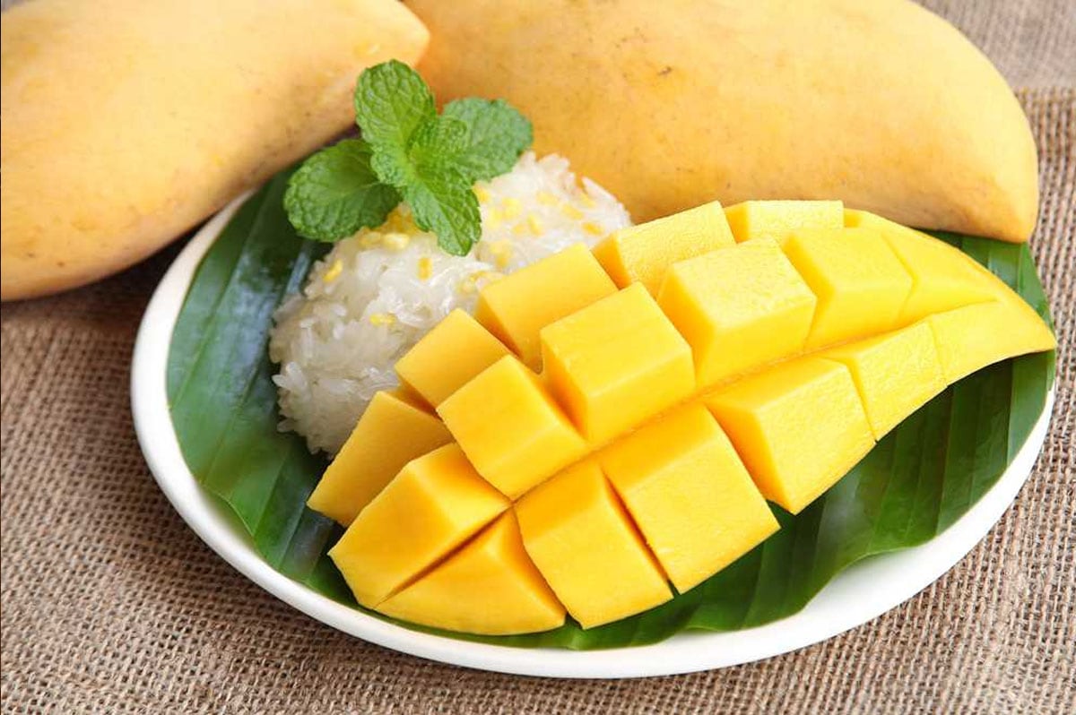 Peeled mango cut into cubes with sticky rice on side and mint leaves