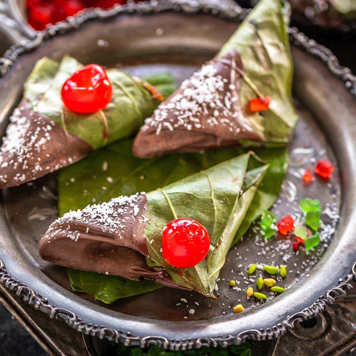 3 chocolate paan topped with cherries and placed in a antique plate