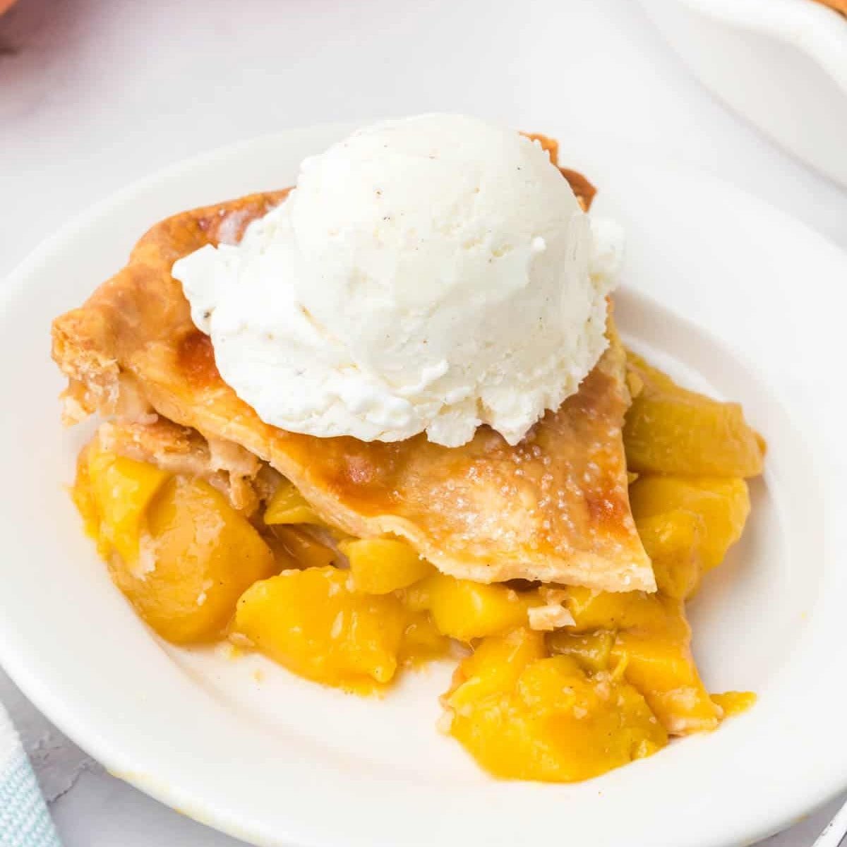 A slice of peach mango pie on a white plate, topped with a scoop of vanilla ice cream. 