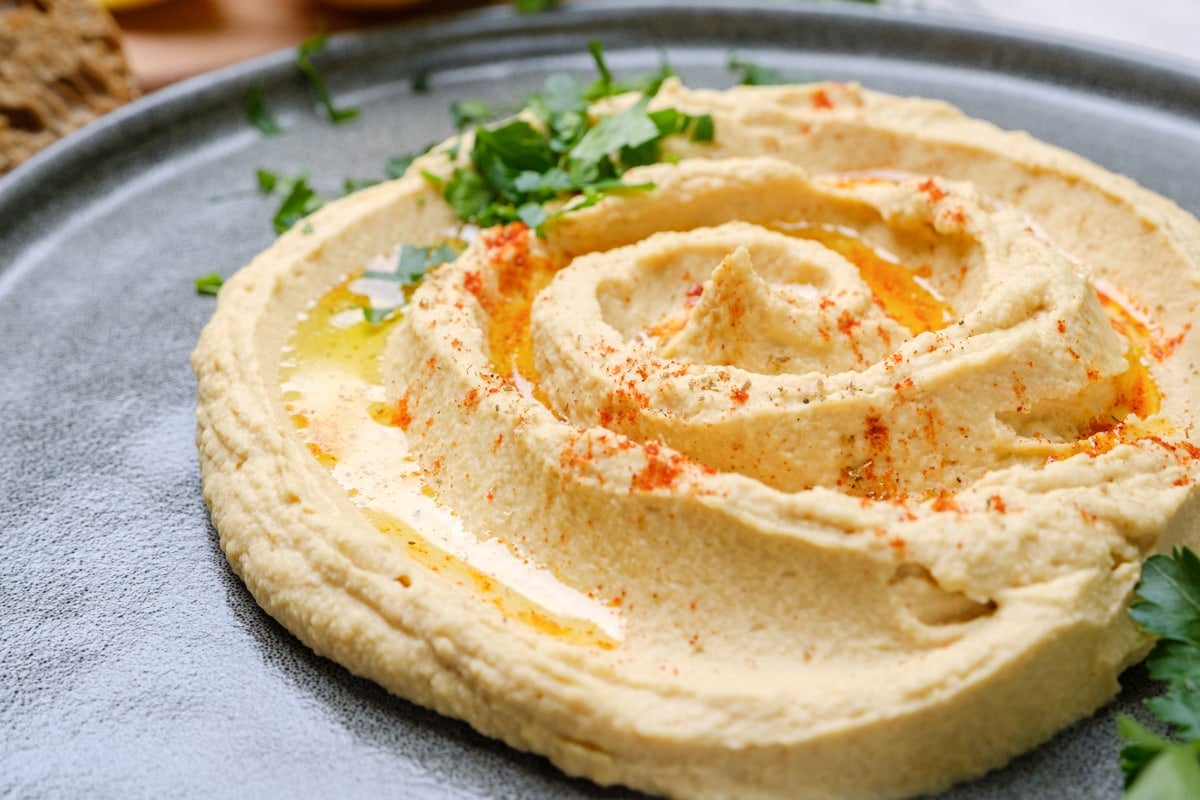 A plate of hummus and pita bread on the side, garnished with paprika and herbs.