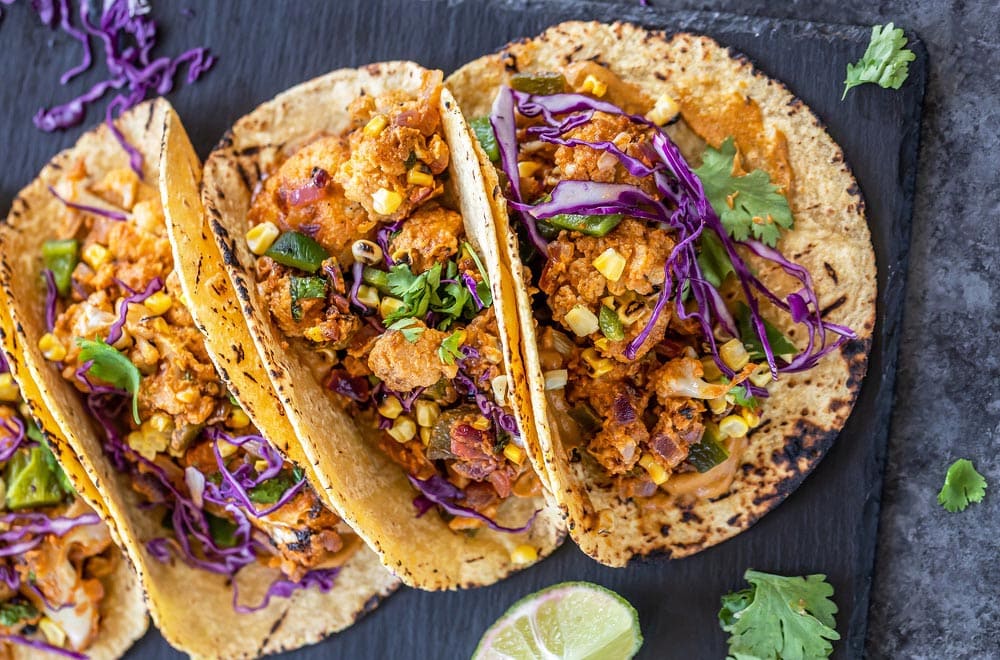 3 tacos filled with cauliflower, topped with cilantro and arranged on a black board