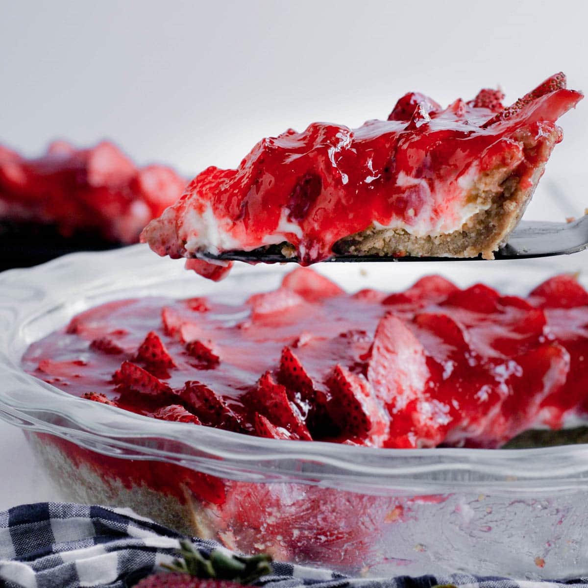 A slice of fresh strawberry pie with a cream cheese filling and a gluten-free graham cracker crust is being served.