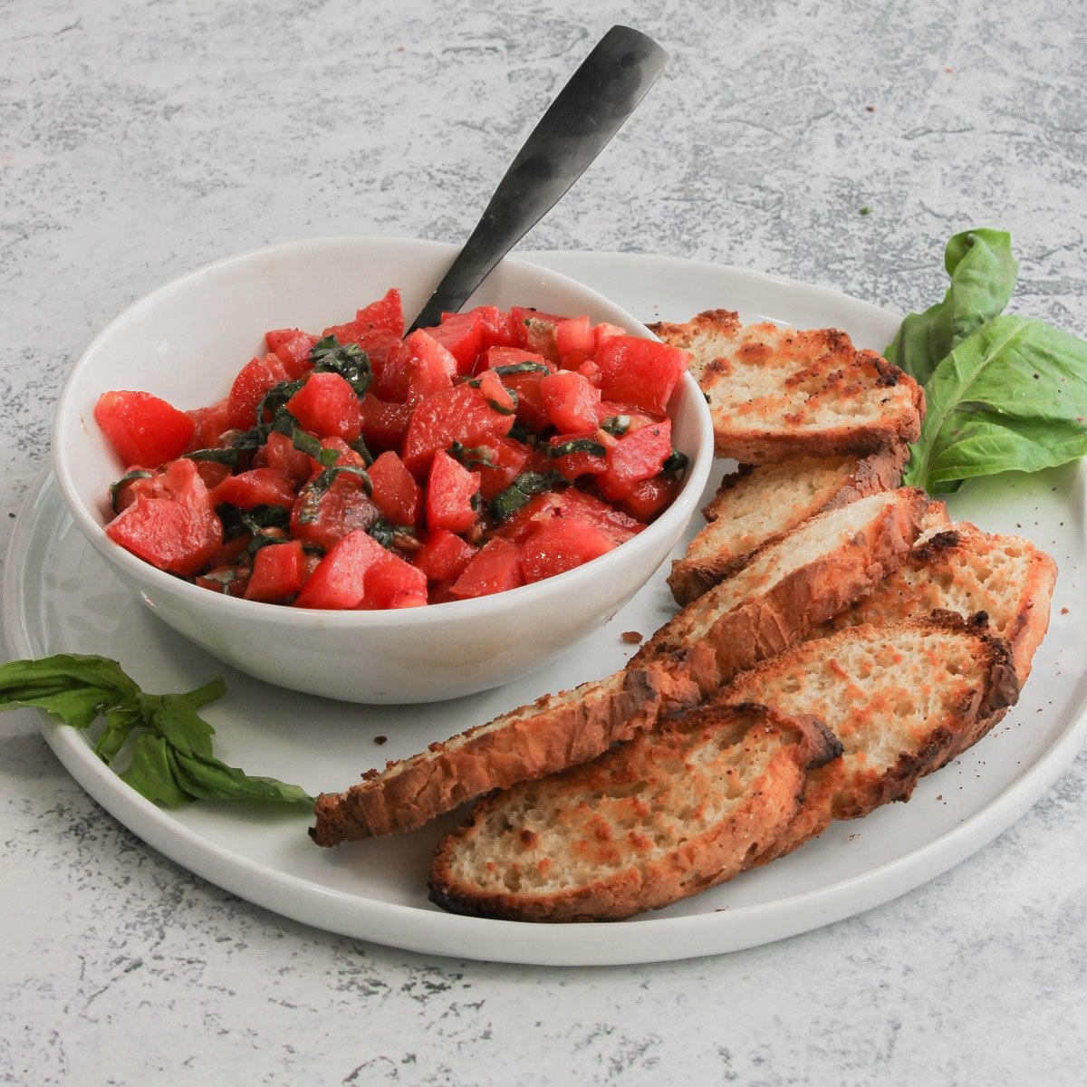 A bowl of tomato bruschetta being served with slices of toasted bread.