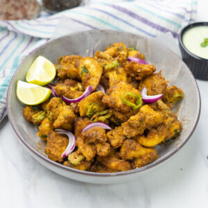 Crispy chicken pakoras in a bowl garnished wit sliced onions and lime wedges.