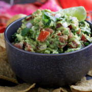 Close up shot of Chunky Spicy Guacamole in a bowl with some chips on side