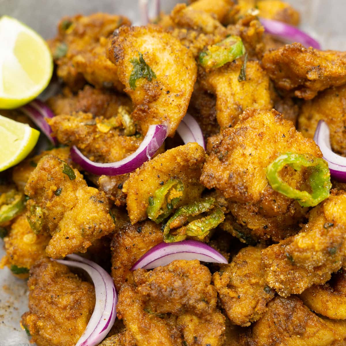 Crispy Chicken Pakora garnished with sliced red onions and lime.
