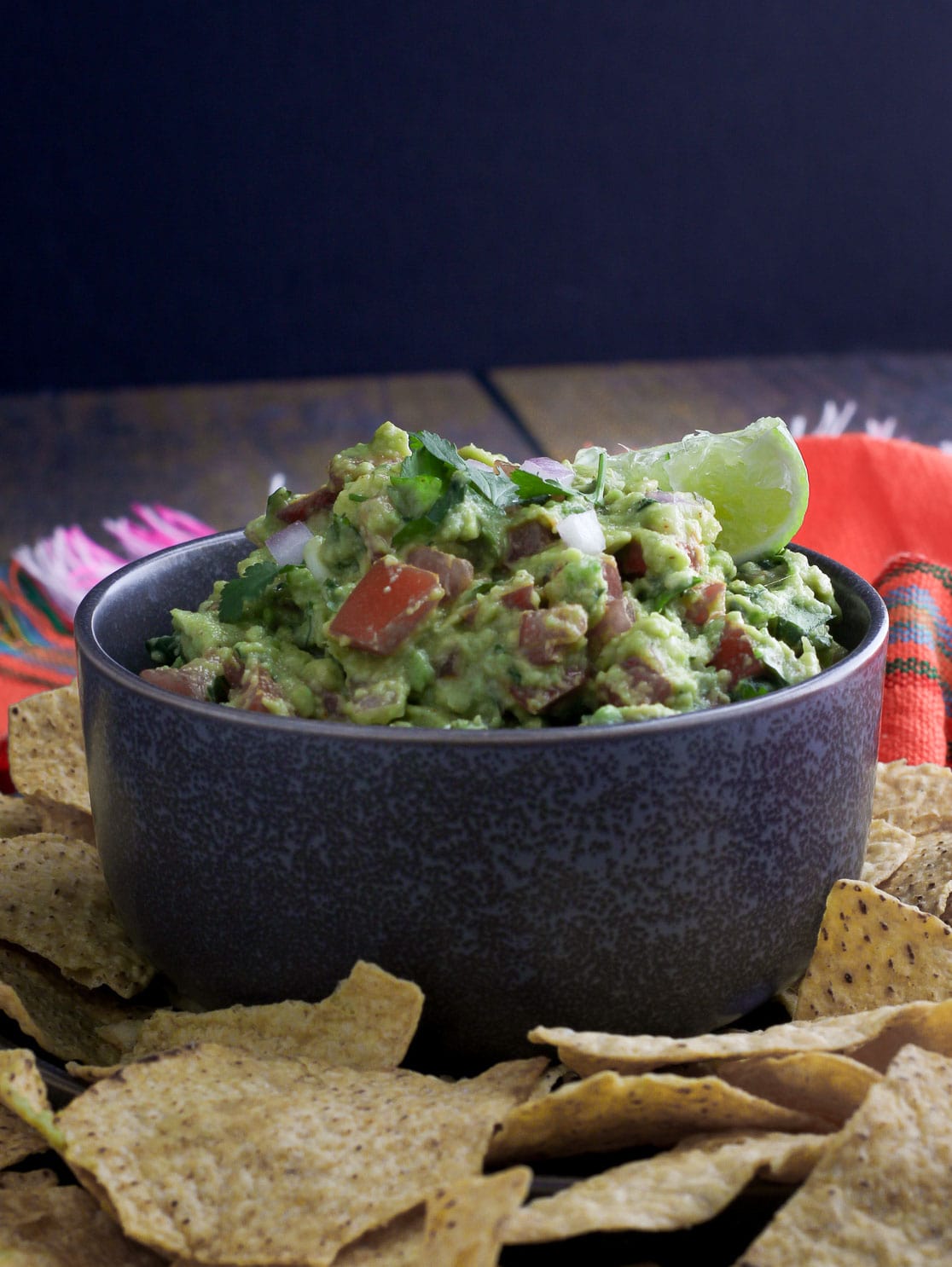 Spicy Chunky Guacamole garnished with cilantro and lime in a bowl with chips on side