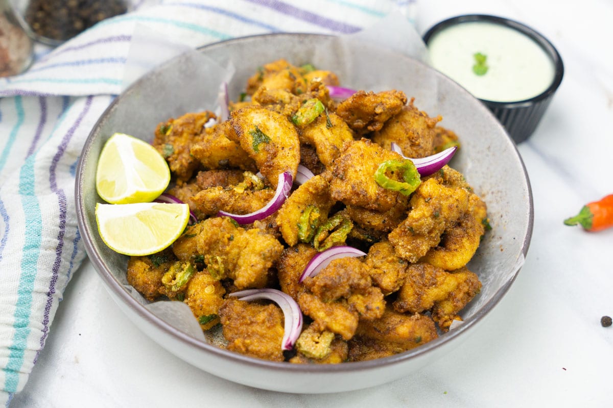 A bowl of chicken pakora garnished with red onions and lime.