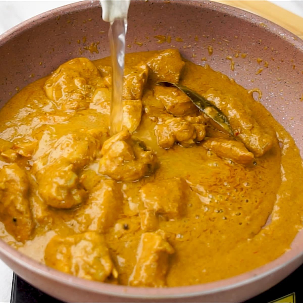 Adding water to chicken in pan to make mughlai chicken curry