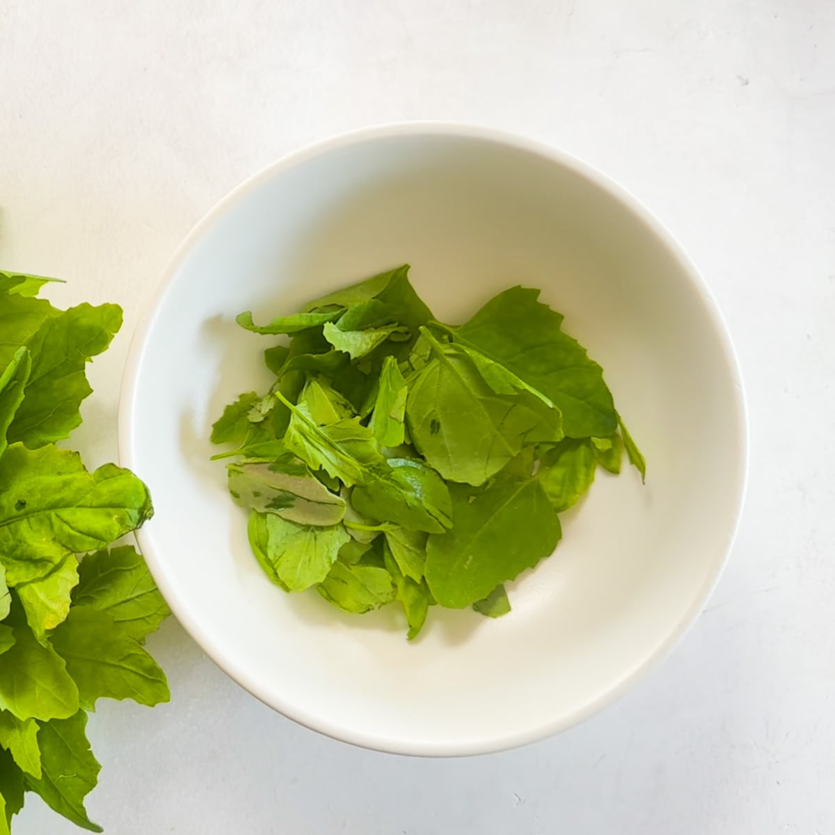 Bathua leaves plucked and put in a white bowl. 