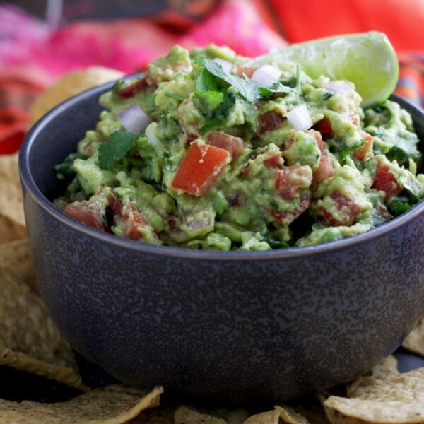 Spicy Chunky Guacamole garnished with cilantro and lime in a bowl with chips on side