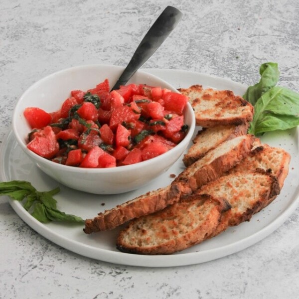 A bowl of tomato bruschetta being served with slices of toasted French bread