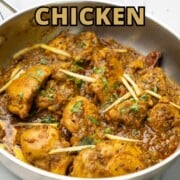 Achari chicken in a pan garnished with julienned ginger and cilantro.
