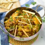 Achari chicken curry in a bowl garnished with julienned ginger and cilantro