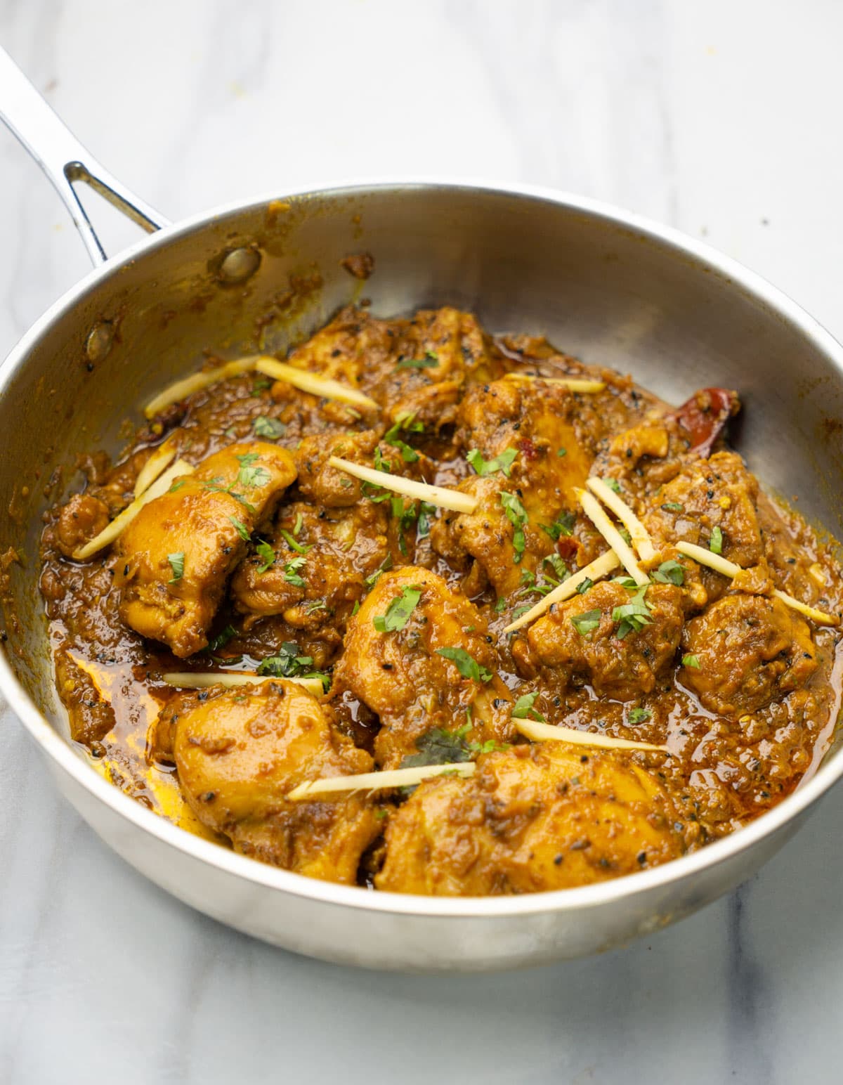 Achari chicken in a pan garnished with julienned ginger