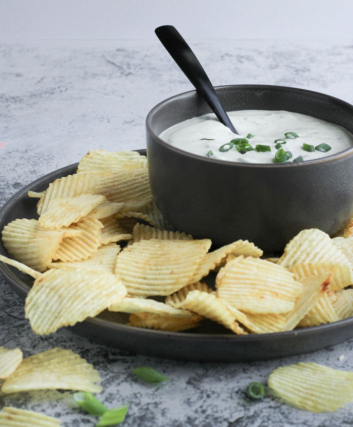 Cream cheese green onion dip in a black bowl with chips around it.