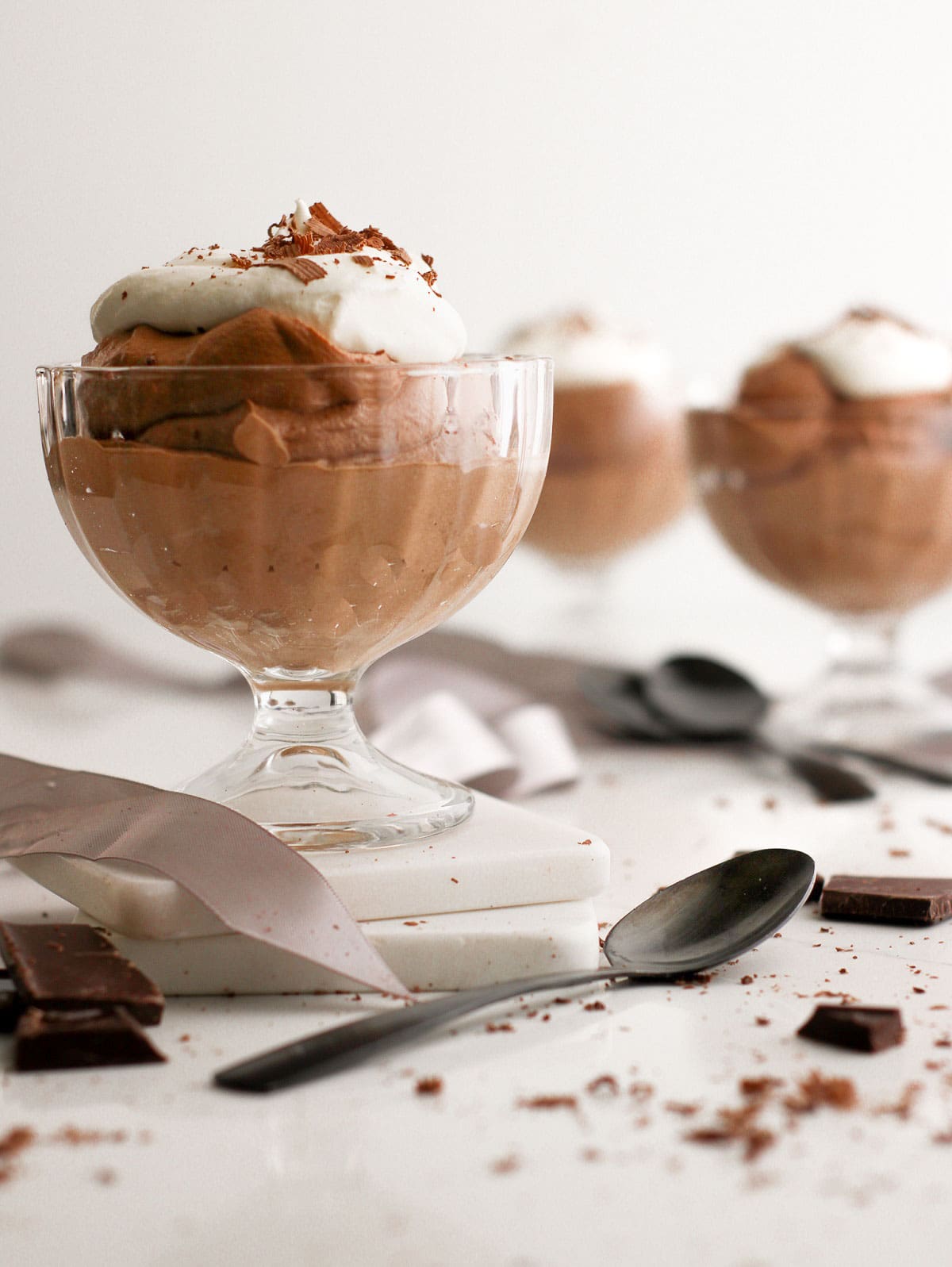 Homemade chocolate mousse in a glass serving dish with a dollop of whipped cream and shaved chocolate on top.