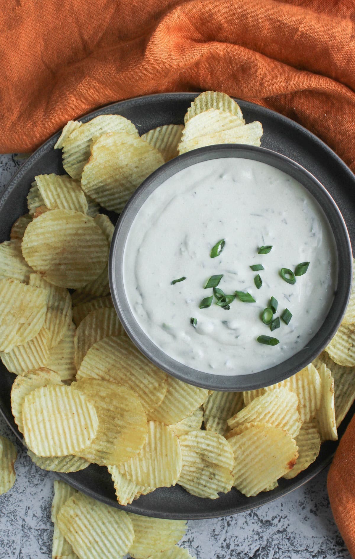 Green onion dip in a bowl garnished with some chopped onions and chips spread around the bowl.