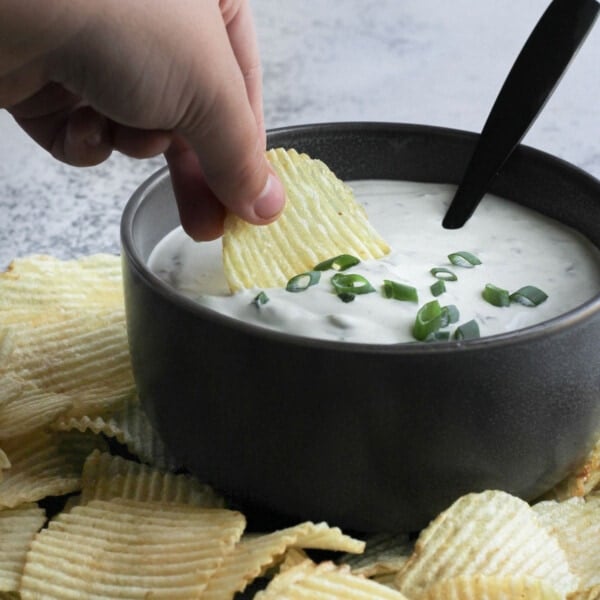 Green onion dip made with cream cheese and sour cream served in a bowl with chips around it.