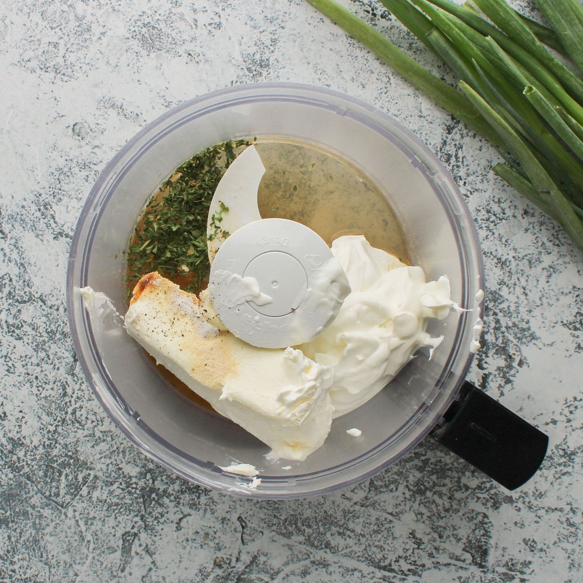 Cream cheese, sour cream, and seasoning added to a food processor to make a green onion dip.