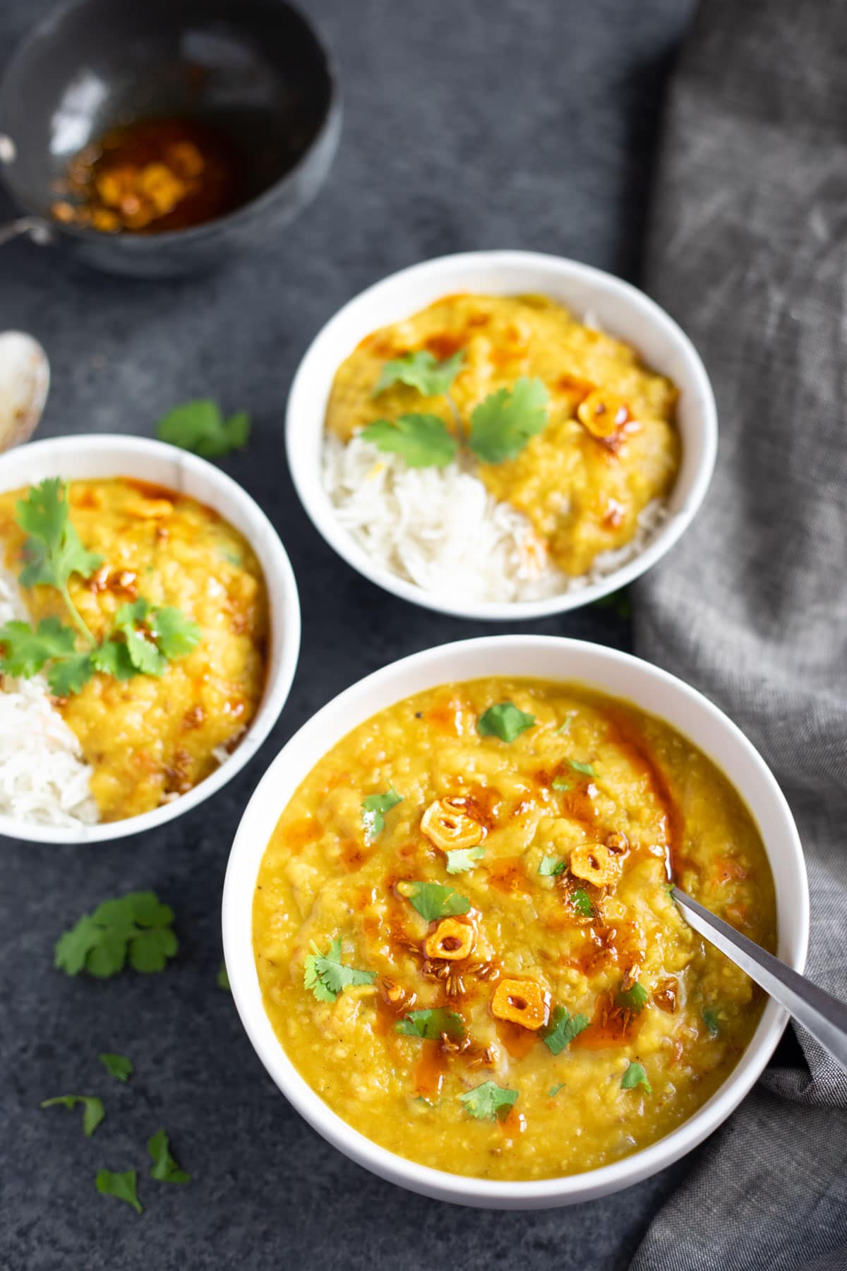 A bowl of red lentil masoor dal garnished with cilantro and another two bowl with rice.