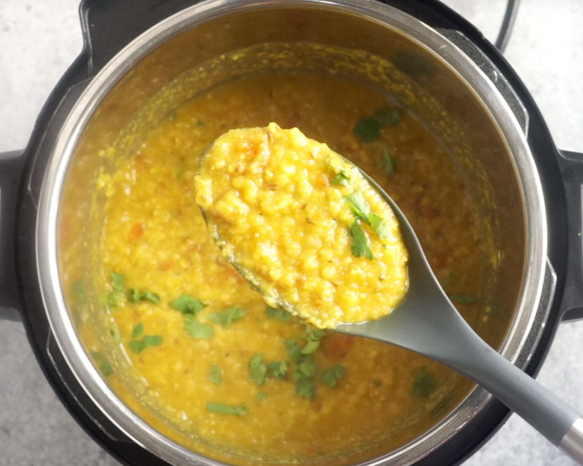 Red lentil dal in a plastic ladle over the instant pot