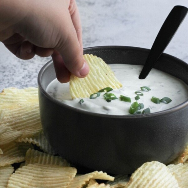 Green onion dip (Scallion dip) served in a bowl with a chip being dipped in it.