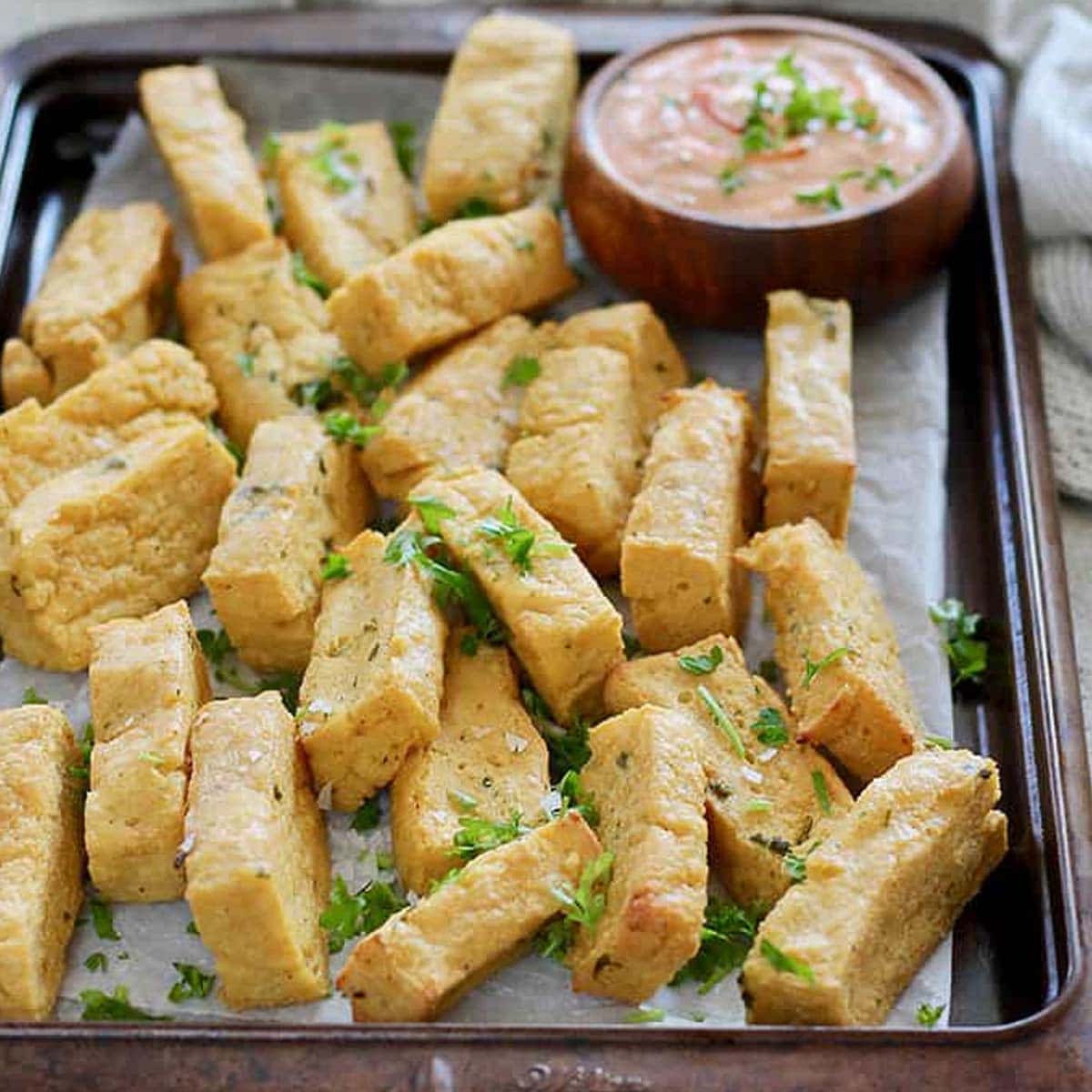 Chickpea fries on a baking sheet scattered with fresh herbs
