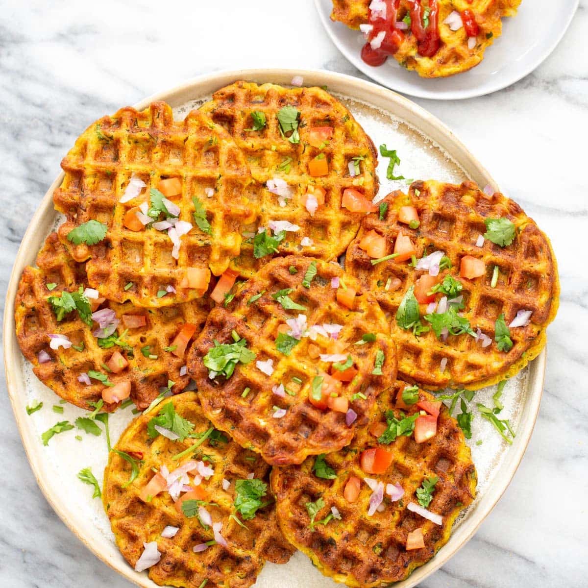 overhead shot of a plate of crispy pakora chickpea flour waffles topped with fresh onions and herbs