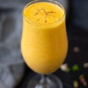 Mango lassi in a tall glass garnished with saffron