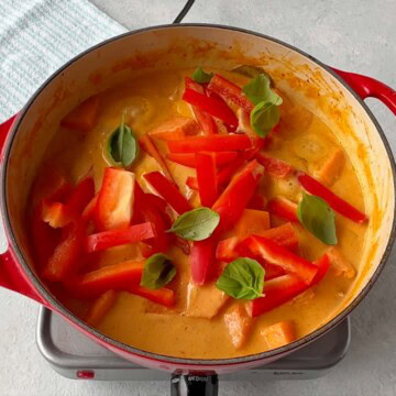 Red Pepper and basil leaves added to pumpkin chicken curry in fry pan.