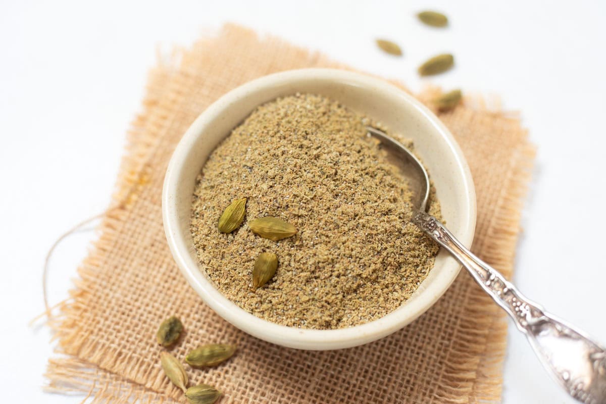 cardamom powder in a white small bowl with silver spoon