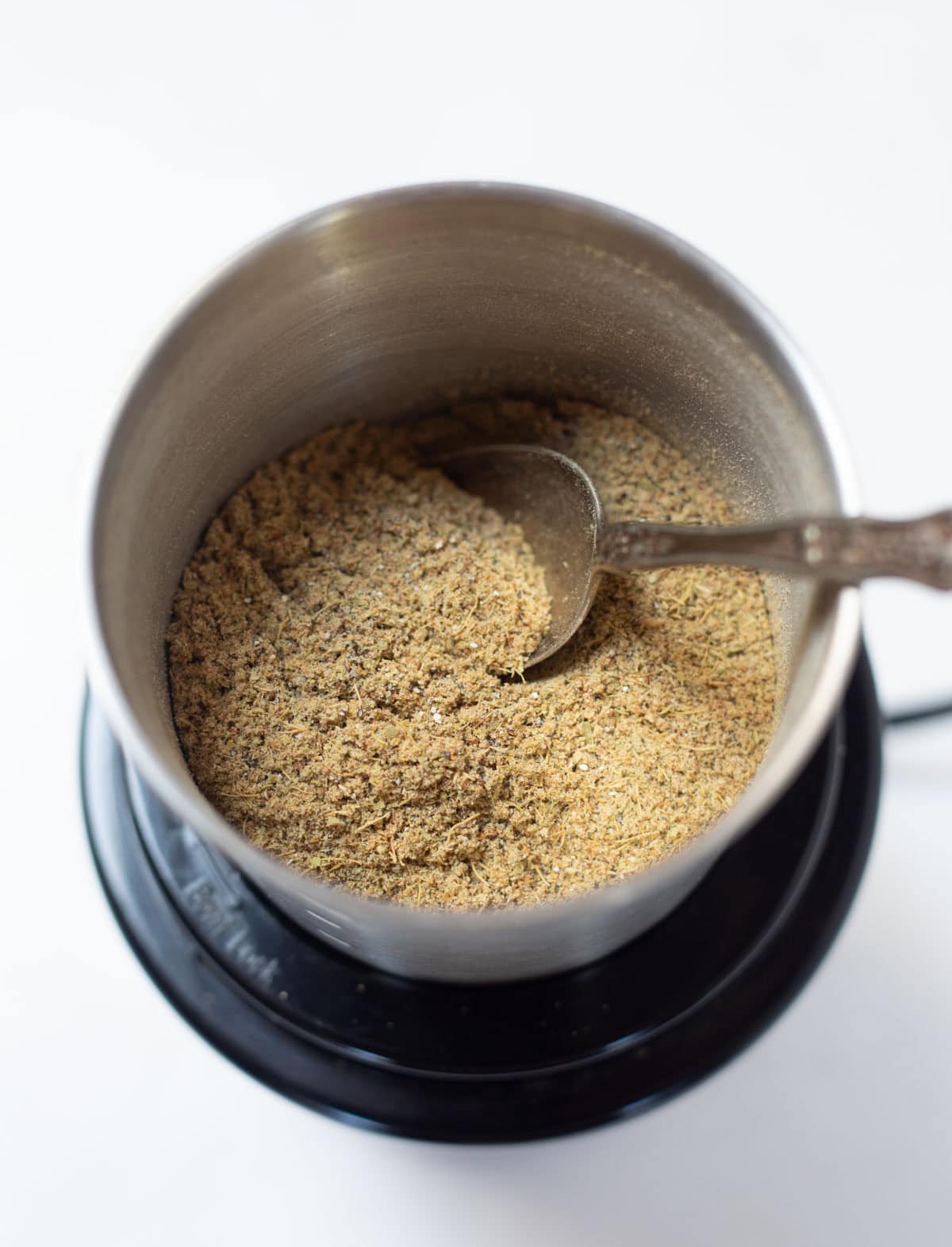 cardamom powder in a spice grinder with silver spoon