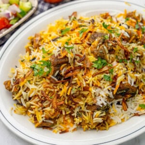 A close-up of a platter with fluffy saffron rice, tender pieces of mutton, and garnished with coriander leaves and fried onions.