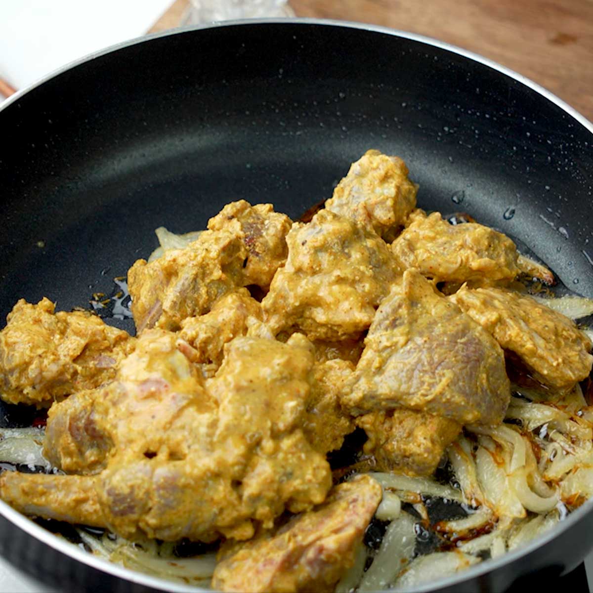 Marinated mutton pieces sizzling in a pan