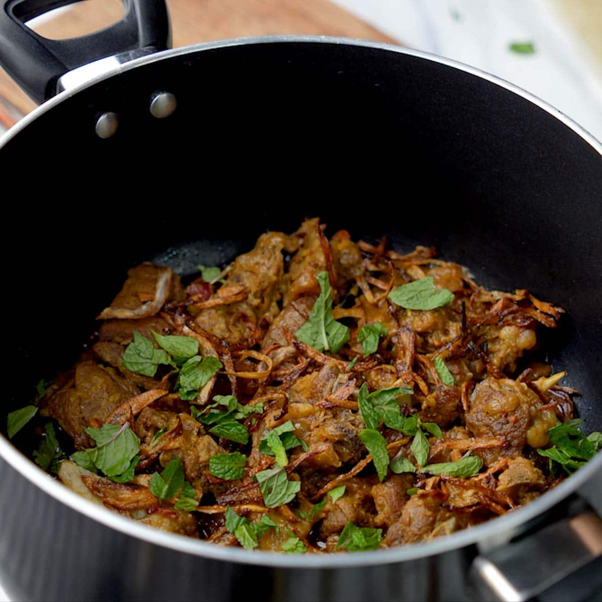 cooked mutton pieces in a pan garnished with mint leaves