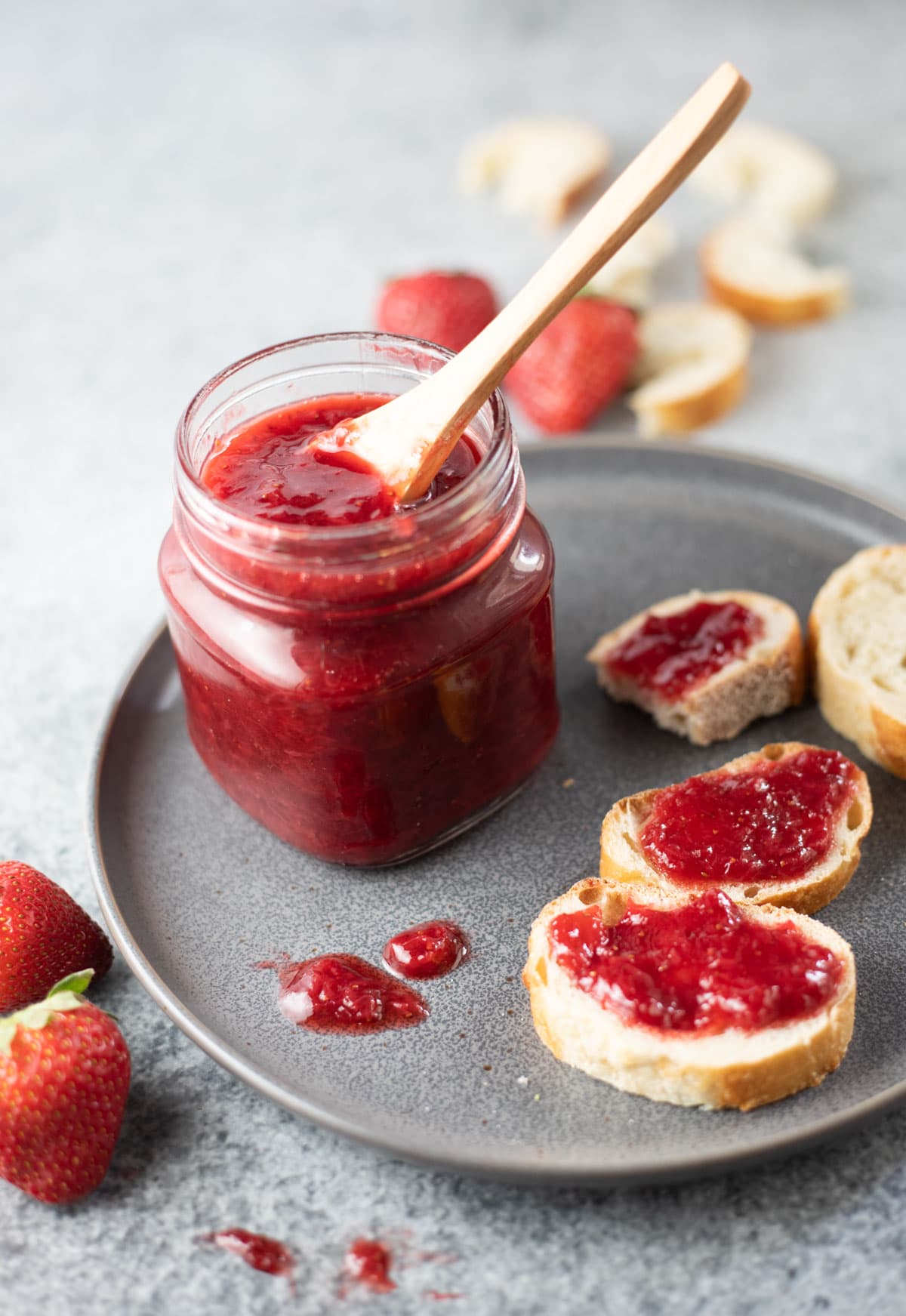 Strawberry Jam in a glass jar on a plate, along with jam spread on sliced bread