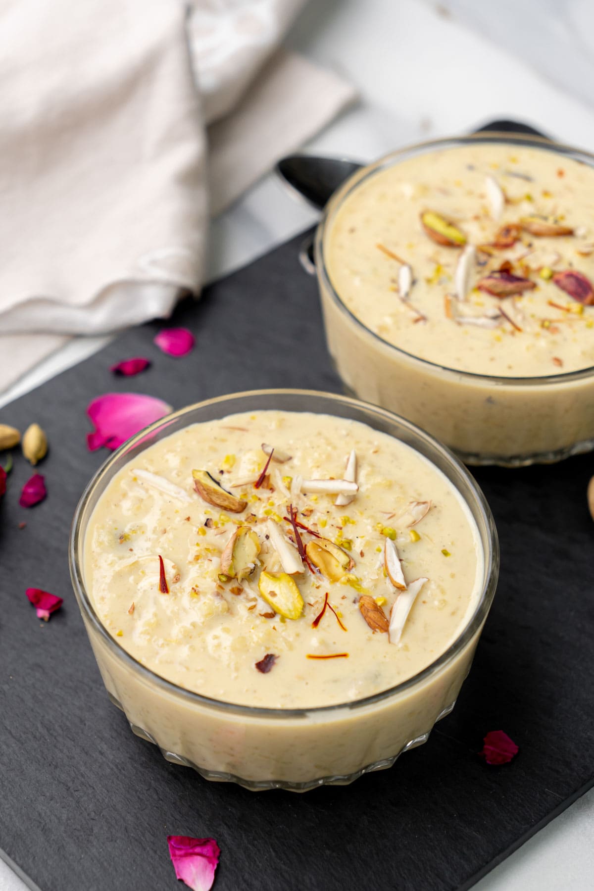 Kheer served in two bowls garnished with nuts and saffron. 