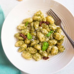 pesto Gnocchi in a white plate garnished with basil leaves and parmesan cheese